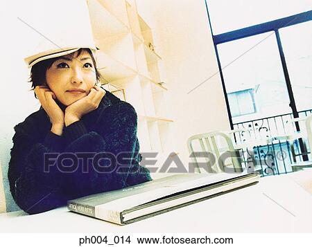 Young woman sitting on table in room, book on table View Large Photo Image Picture - Young woman sitting on table in room, book on table . Fotosearch