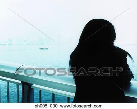 Stock Image - Woman leaning against railing, silhouette, rear view. Fotosearch