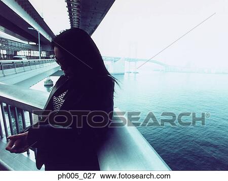 Stock Photo - Woman leaning against railing, silhouette, portrait. Fotosearch