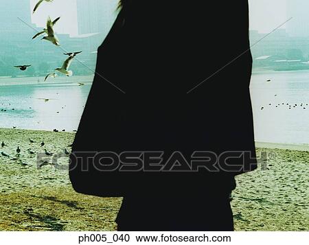 Woman standing on beach, seagulls flying, silhouette View Large Photo Image Stock Image - Woman standing on beach, seagulls flying, silhouette. Fotosearch