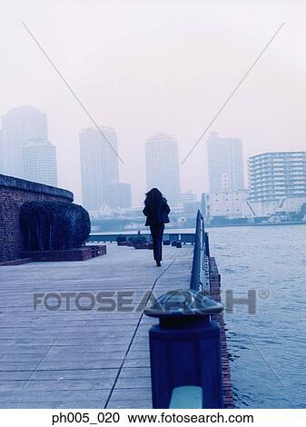 Woman walking along jetty, Tokyo city in background View Large Photo Image Stock Image - Woman walking along jetty, Tokyo city in background. Fotosearch