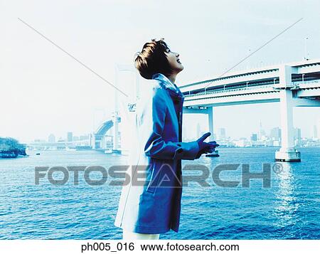 Stock Photograph - Young woman at waterfront, bridge in background. Fotosearch