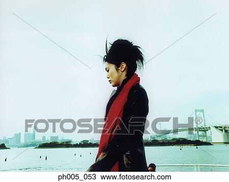 Stock Image - Young woman at waterfront, city in background. Fotosearch