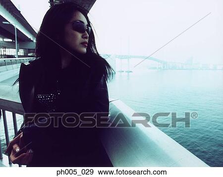 Stock Photo - Young woman leaning against railing, close up, portrait. Fotosearch