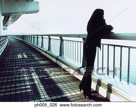 Stock Photograph - Young woman leaning against railing, under the bridge. Fotosearch