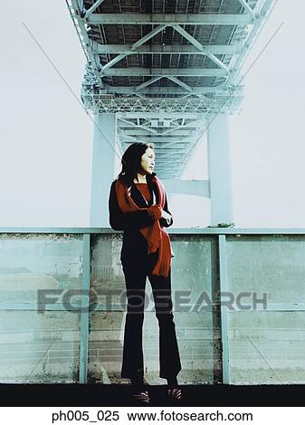 Stock Photography - Young woman leaning against railing, under the bridge. Fotosearch