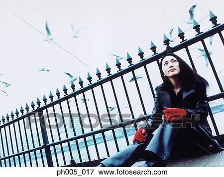 Stock Photo - Young woman sitting against railing, Tokyo city in background, a flock of seagulls. Fotosearch