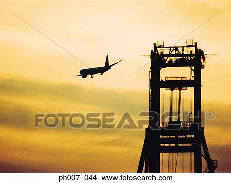 Passenger aircraft flying over port at sunset View Large Photo Image Picture - Passenger aircraft flying over port at sunset. Fotosearch