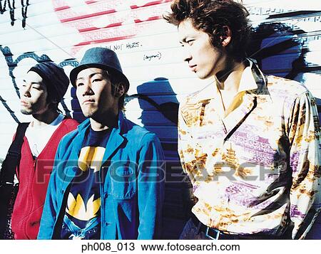 Stock Image - Three young men leaning against vandalized wall. Fotosearch