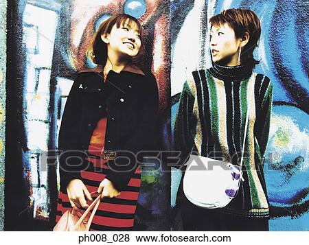 Two young women standing against vandalized wall View Large Photo Image Stock Photo - Two young women standing against vandalized wall. Fotosearch