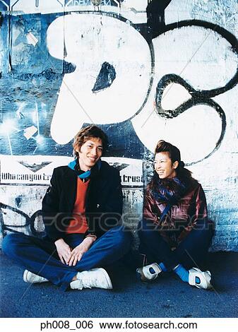 Stock Photograph - Young couple sitting against vandalized wall. Fotosearch