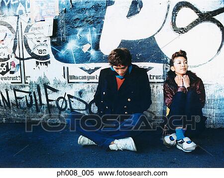 Stock Photography - Young couple sitting against vandalized wall. Fotosearch