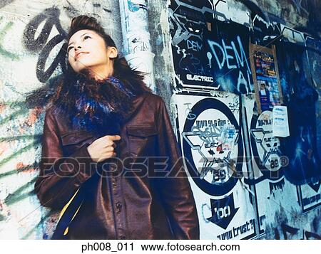 Stock Image - Young woman leaning against vandalized wall. Fotosearch