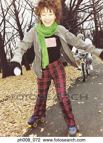 Stock Image - Young woman roller blading in a park. Fotosearch