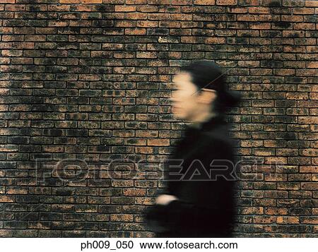 Stock Image - Young woman walking, in front of Brick Wall (blurred motion). Fotosearch