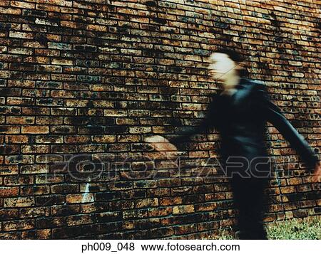 Stock Photo - Young woman walking, in front of Brick Wall (blurred motion). Fotosearch