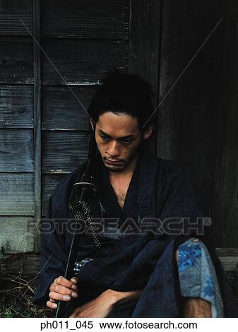 Samurai warrior sitting against a house holding a sword View Large Photo Image Stock Photography - Samurai warrior sitting against a house holding a sword. Fotosearch
