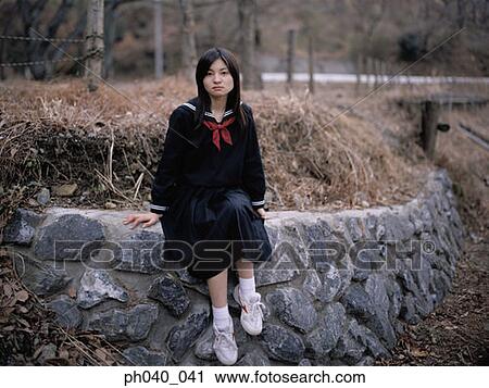Stock Image - School girl sitting on a rock divider. Fotosearch
