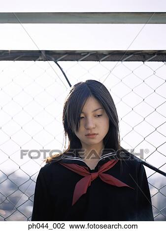 Stock Image - School girl leaning against a fence. Fotosearch