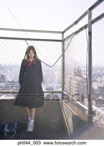 Stock Image - School girl leaning against a fence. Fotosearch
