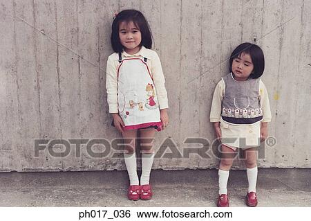 Two sisters leaning against the wall View Large Photo Image Stock Photograph - Two sisters leaning against the wall. Fotosearch