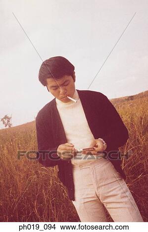 Picture - Portrait of a young Asian man lighting a cigarette. Fotosearch