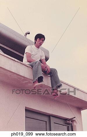 Stock Photo - Portrait of a young Asian man sitting on the roof top. Fotosearch