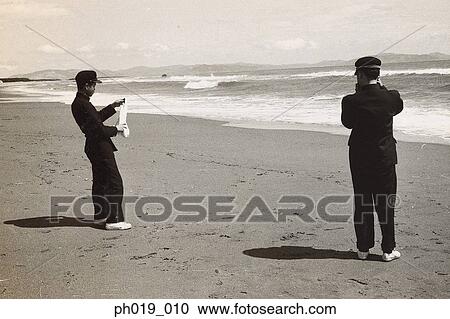 Stock Image - Two Asian men in uniform at the beach. Fotosearch