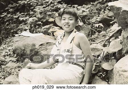 Stock Photo - Young Asian man sitting on the rocks. Fotosearch