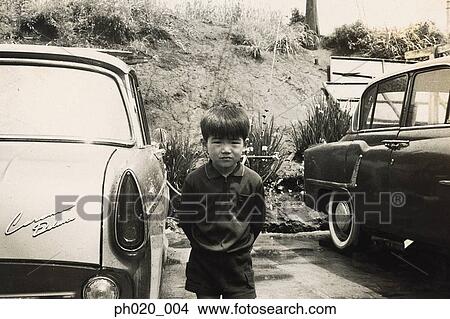 Picture - Boy standing between two cars. Fotosearch