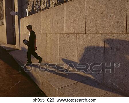 Young male walking holding skateboard View Large Photo Image Stock Image - Young male walking holding skateboard . Fotosearch