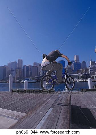 Young man performing bike stunt on jetty View Large Photo Image Picture - Young man performing bike stunt on jetty. Fotosearch