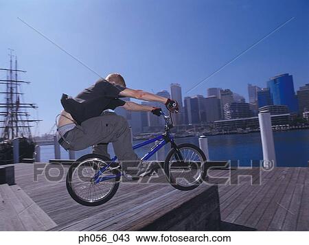 Young man performing bike stunt on jetty View Large Photo Image Stock Image - Young man performing bike stunt on jetty. Fotosearch