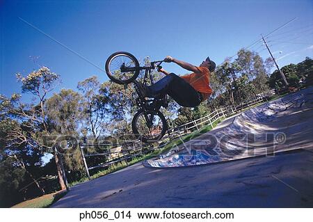 Picture - Young man performing bike stunt on ramp. Fotosearch