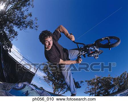 Young man performing bike stunt on ramp View Large Photo Image Stock Image - Young man performing bike stunt on ramp. Fotosearch