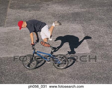 Young man performing bike stunt on pavement View Large Photo Image Stock Image - Young man performing bike stunt on pavement. Fotosearch