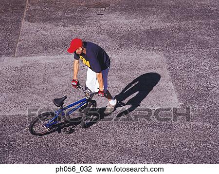 Young man performing bike stunt on pavement View Large Photo Image Stock Image - Young man performing bike stunt on pavement. Fotosearch
