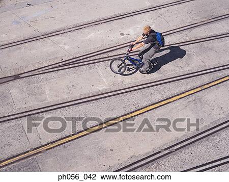 Stock Image - Young man performing bike stunt on pavement. Fotosearch