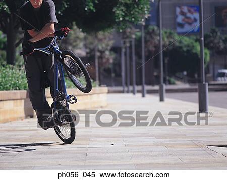 Young man performing bike stunt on pavement View Large Photo Image Stock Photography - Young man performing bike stunt on pavement. Fotosearch