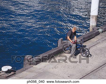 Stock Image - Young man resting on BMX on pavement . Fotosearch