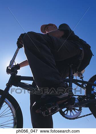 Stock Photo - Young man resting on BMX on pavement, low angle view. Fotosearch