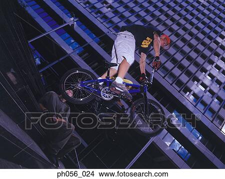 Picture - Young men in mid-air jump on bike, city scene. Fotosearch