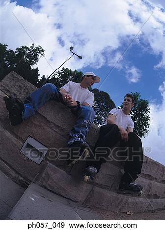 Stock Photo - Portrait of two in-line skaters sitting on platform. Fotosearch