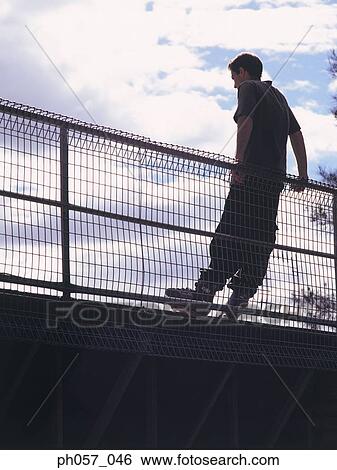 Stock Photograph - Young in-line skater leaning against railing, portrait . Fotosearch