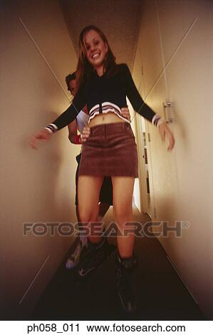 Stock Image - Teenage girl learns skating, boy supports her from behind. Fotosearch
