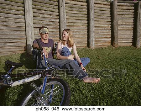 Stock Photograph - Young couple sitting together on grass talking . Fotosearch