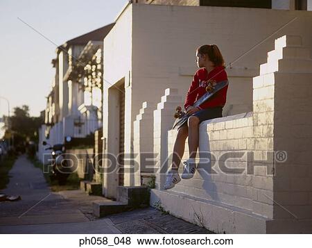 Young girl sitting on stone wall with a skateboard View Large Photo Image Stock Photo - Young girl sitting on stone wall with a skateboard. Fotosearch