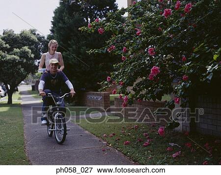 Young man cycling with young woman on back of bike View Large Photo Image Stock Photo - Young man cycling with young woman on back of bike . Fotosearch