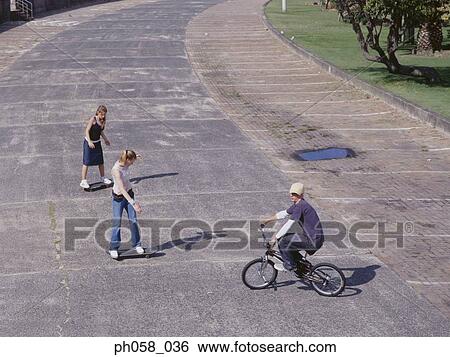 Young man cycling, young women skateboarding View Large Photo Image Stock Photograph - Young man cycling, young women skateboarding. Fotosearch