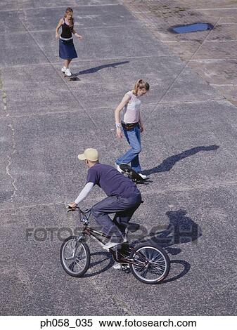 Young man cycling, young women skateboarding View Large Photo Image Stock Photography - Young man cycling, young women skateboarding. Fotosearch